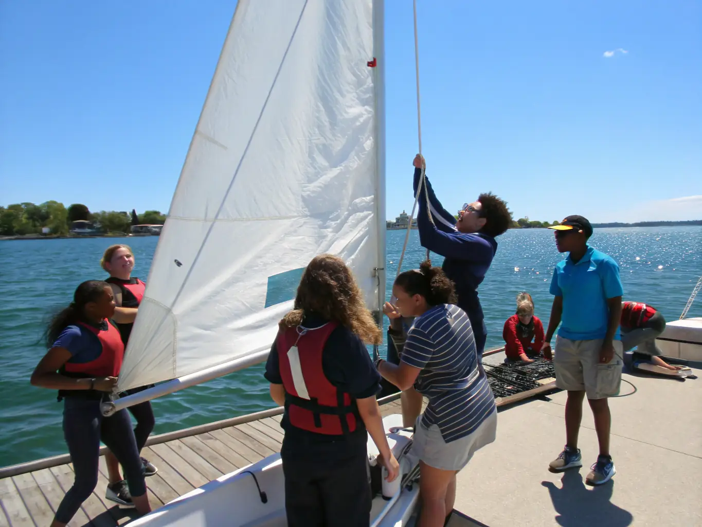 A vibrant image of children participating in a beginner sailing lesson, with instructors nearby providing guidance and support, set against a sunny, clear day on the water.